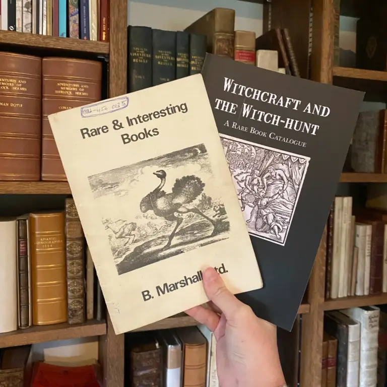 Two catalogues held in front of bookshelves: Rare & Interesting Books and Witchcraft and the Witch-hunt